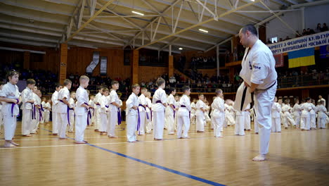 male karate coach shows the moves with legs to his numerous trainees. young sportsmen repeat the exercise after the trainer.