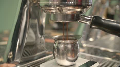 Portafilter-attached-to-stainless-steel-espresso-machine-drips-into-silver-pitcher