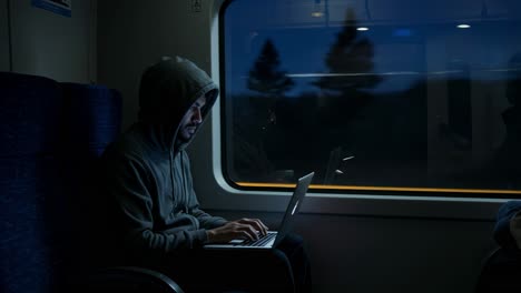 A man diligently types away on his laptop late at night while riding a train that travels through a bustling urban landscape