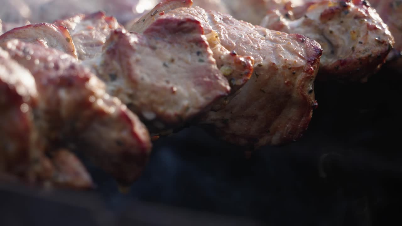 Primo piano di carne di maiale succulenta e marinata con spezie ed erbe aromatiche su braci ardenti su una griglia da barbecue, fumo al rallentatore.