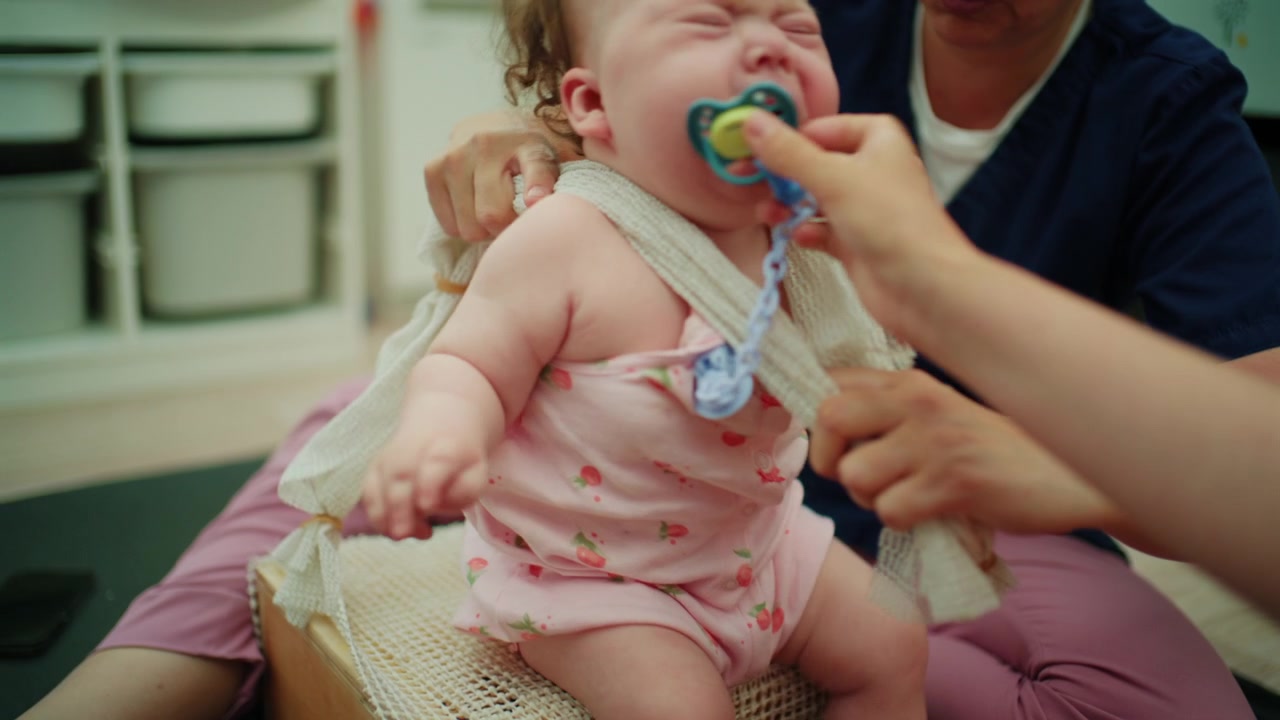 Bebê sentindo desconforto durante uma sessão de reabilitação enquanto um fisioterapeuta auxilia, promovendo a recuperação e o desenvolvimento precoce.