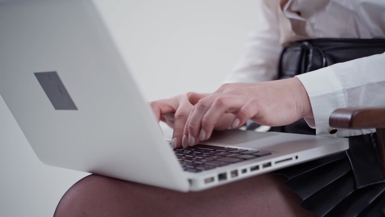 Modern laptop on female's legs. Young woman's hands typing on a white laptop. Close-up. Slow motion.
