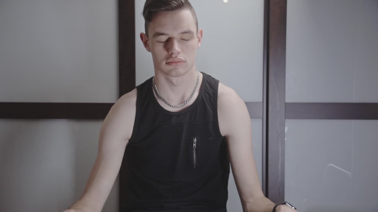 로터스 요가 위치에 앉아 집에서 자신의 방 안에서 명상하는 젊은 남자