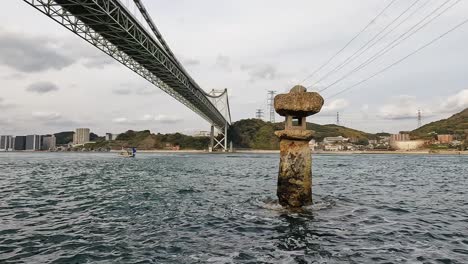 beautiful old japanese rock lantern halfly submerged in water in front of kanmon bridge and the kanmon strait in between the japanese island honshu and kyushu