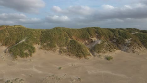 a drone orbits from right to left in a over the beach, capturing sand being swept across the dunes at hvide sande