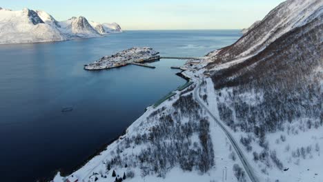 vista de avión no tripulado en las montañas de tromso en invierno lleno de nieve que muestra husoy una pequeña ciudad en una isla rodeada por el mar y su pequeño puerto con gaviotas voladoras