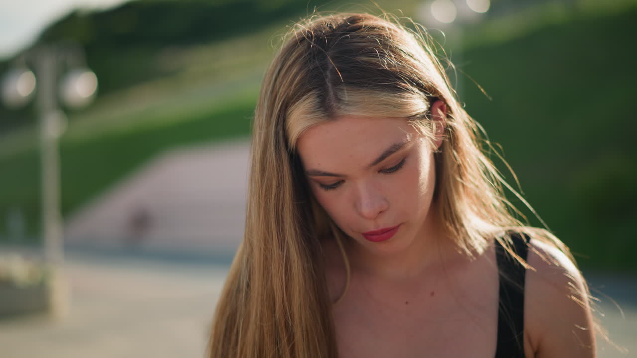 그녀가 아래로 초점을 맞추면서 깊은 생각에 빠진 것처럼 보이는 사려 깊은 여인, 배경에는 초록색과 흐릿한 램프 기둥이 있습니다.