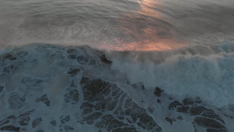 flying backwards over an ocean at sunset, tilting down, following a big rolling wave