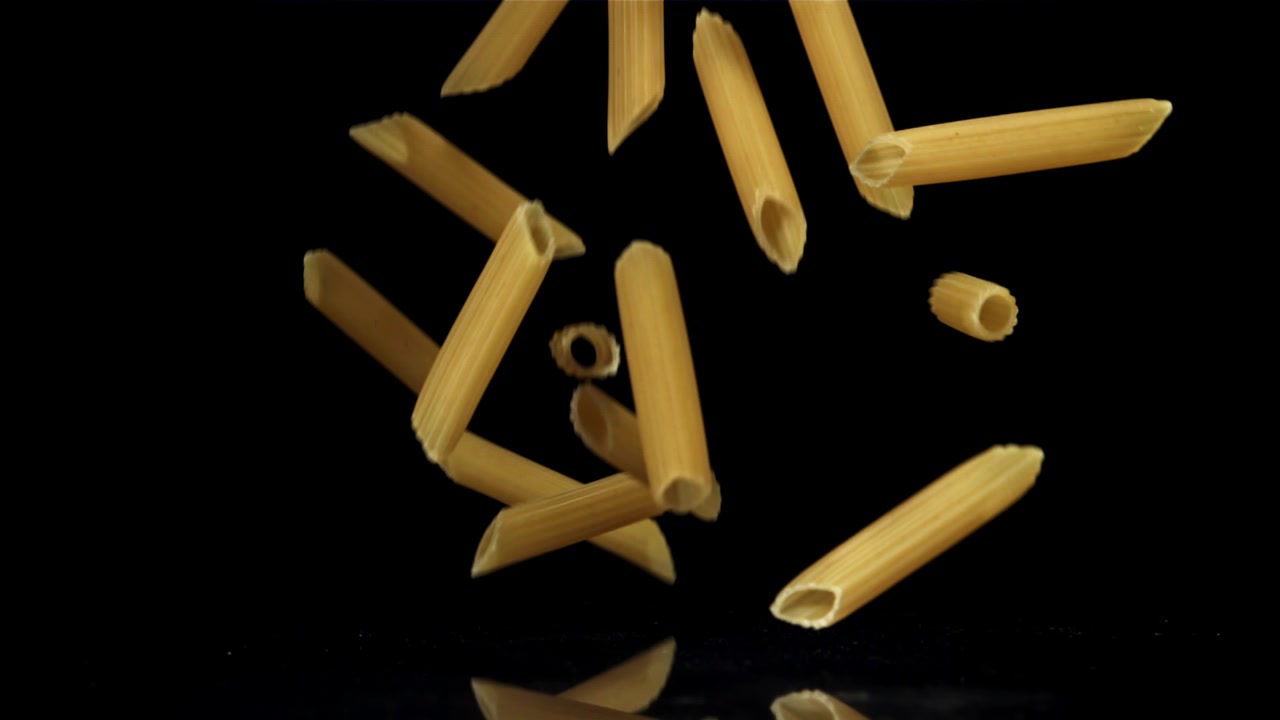 Rohe Penne-Nudeln fallen in Zeitlupe vor schwarzem Hintergrund