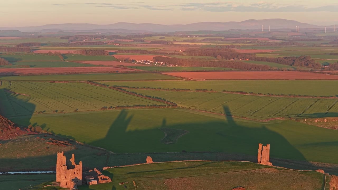Riprese aeree con drone che rivelano le rovine storiche del castello di Dunstanburgh sulla costa del Northumberland durante una spettacolare alba dorata.