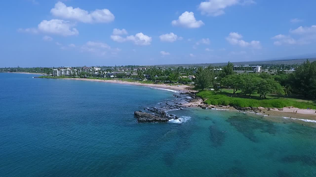 Great cliffs washed by blue turquoise sea water on shore of tropical island with holiday resorts surrounded by trees in Hawaii