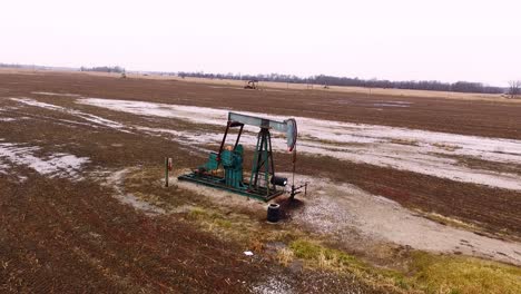 a steady overhead shot from a drone of a pump jack collecting oil from an oilfield in a field during the winter