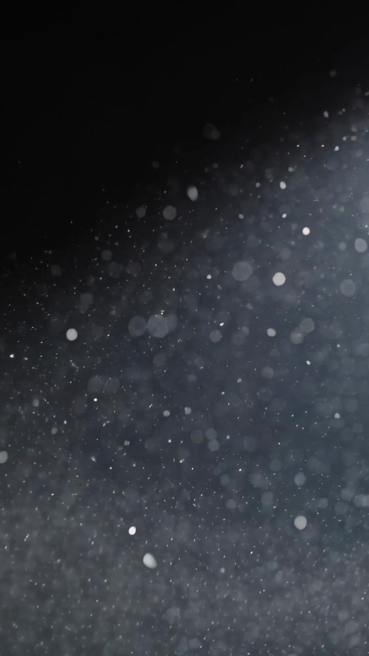 Video verticale: Fascio di luce che illumina dall'alto a destra, illuminando particelle fluttuanti nello spazio buio, con effetto bokeh