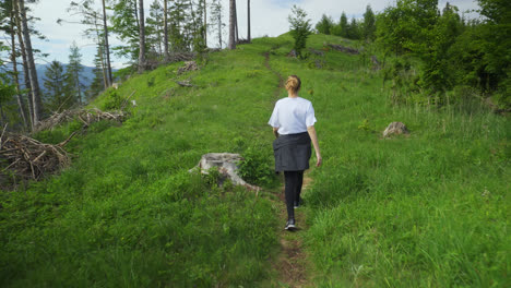 back view of female hiker walking in the mountain trail at summer. - rear follow