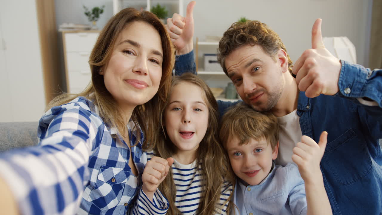 쾌활한 부모와 아이들이 거실 소파에 앉아 포즈를 취하고 카메라에 몸짓을 보여줍니다.