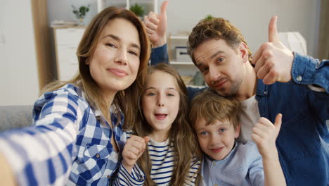 Pov-Of-The-Cheerful-Parents-And-Kids-Sitting-On-The-Couch-In-The-Living-Room,-Posing-And-Showing-Gestures-To-The-Camera