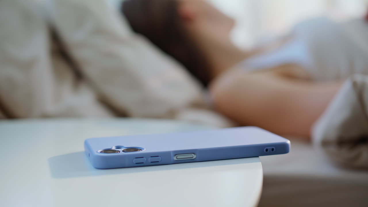 Primo piano di una donna che dorme e che allunga la mano per raggiungere il telefono per svegliarsi in un appartamento. Brunetta che prende