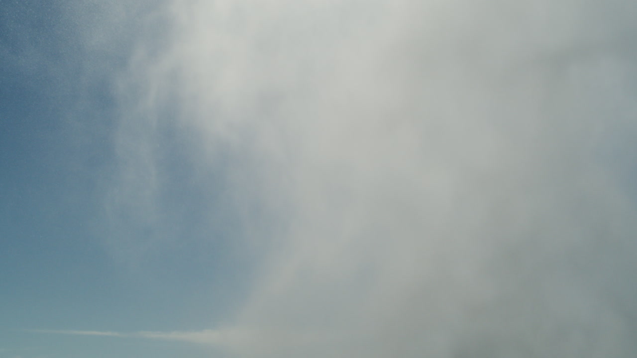 White sea spray erupts skyward in brilliant light against ocean horizon and clear blue sky