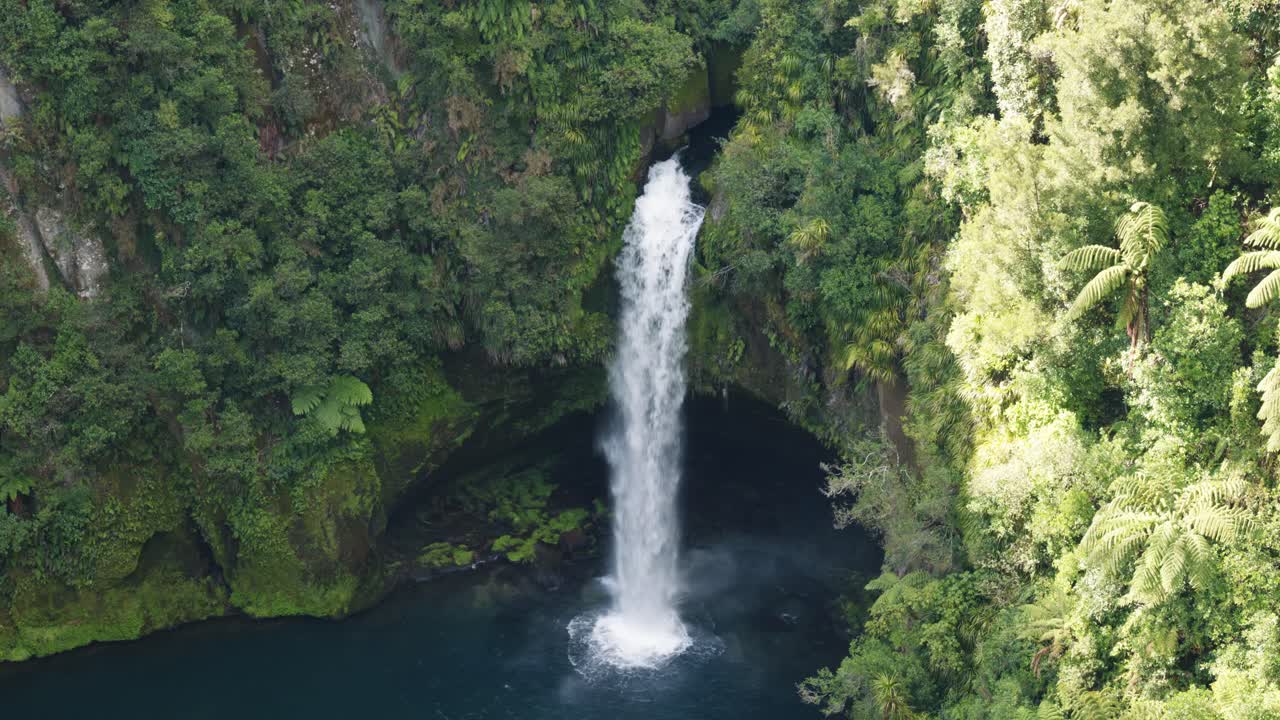 Close view of a waterfall with a lake in between green forest on a sunny day at Omanawa Falls, Tauranga, New Zealand.