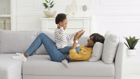 Madre-Bonita-Feliz-Jugando-Juego-De-Manos-Con-Una-Pequeña-Hija-Linda-En-El-Sofá-En-Casa