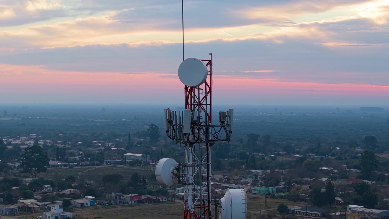 Telecommunications tower with multiple antennas overlooks San Jose de Feliciano and rural outskirts in Feliciano, Entre Rios, Argentina, during evening light, orbiting.