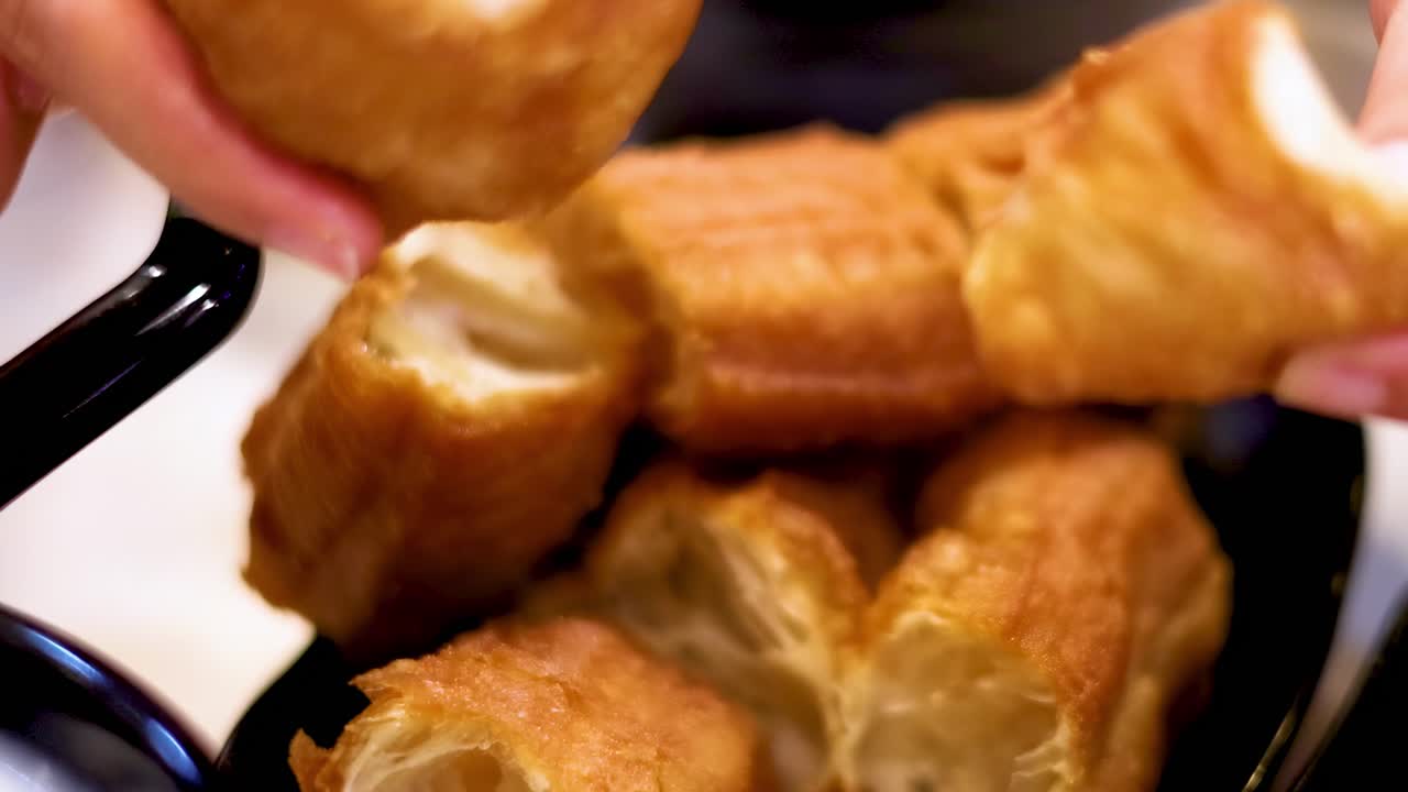 Close-up of hands arranging golden, crispy fried dough pieces in a black bowl.