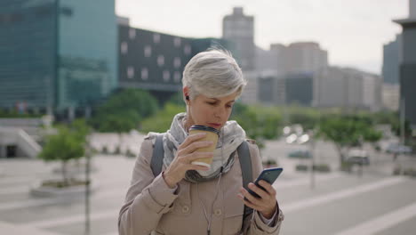 Retrato-De-Una-Mujer-De-Negocios-Caucásica-Madura-Enviando-Mensajes-De-Texto-Navegando-Usando-Las-Redes-Sociales-De-Un-Teléfono-Inteligente-Relajada-Bebiendo-Café-En-Una-Ciudad-Urbana