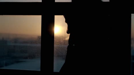 close silhouette of girl looking outside window at sunset