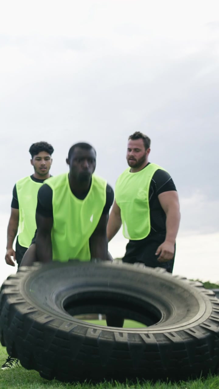 Giocatori di rugby che eseguono esercizi di allenamento con ribaltamento di pneumatici sul campo