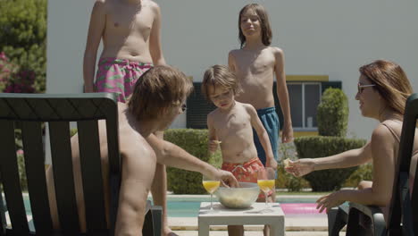 feliz familia caucásica comiendo papas fritas mientras se relaja en el patio trasero cerca de la piscina en un día de verano