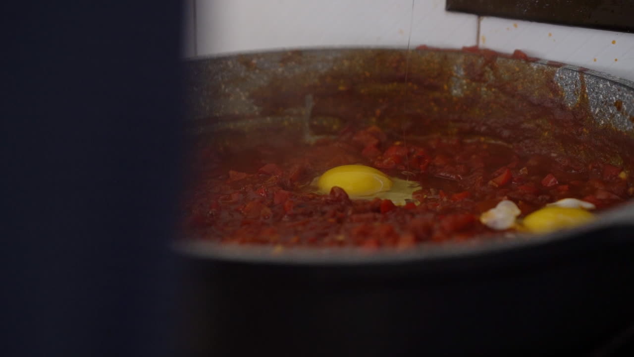 el hombre rompe un huevo en una salsa de tomate burbujeante, preparación de shakshouka casero, filmado en cámara lenta y luz natural del día