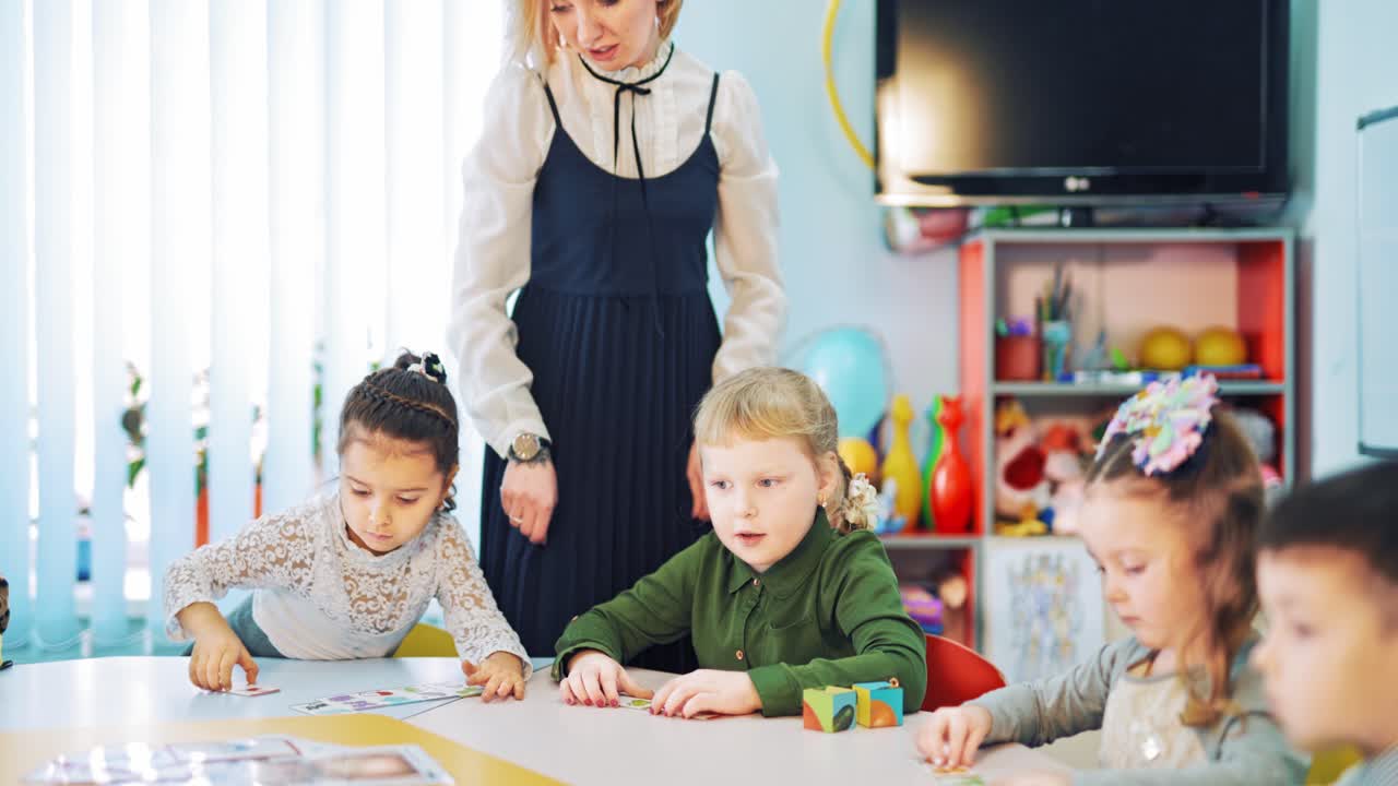 Group of elementary school children and a teacher. Beautiful female teacher helps little children to work with pictures at the classroom.