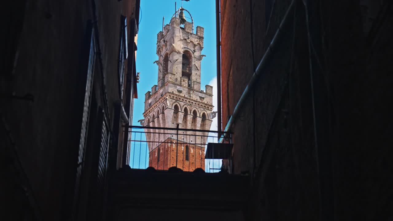 Siena, İtalya'da, Piazza del Campo yakınındaki binalar arasındaki dar bir aralıktan Mangia Kulesi görünüyor