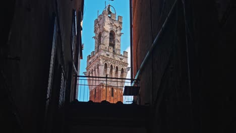 la torre de mangia aparece entre un estrecho hueco en los edificios cerca de la plaza del campo, siena, italia