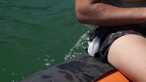 el hombre sumerge la mano en el agua mientras viaja en un bote de goma que acelera sobre el lago en un día soleado - un primer plano extremo