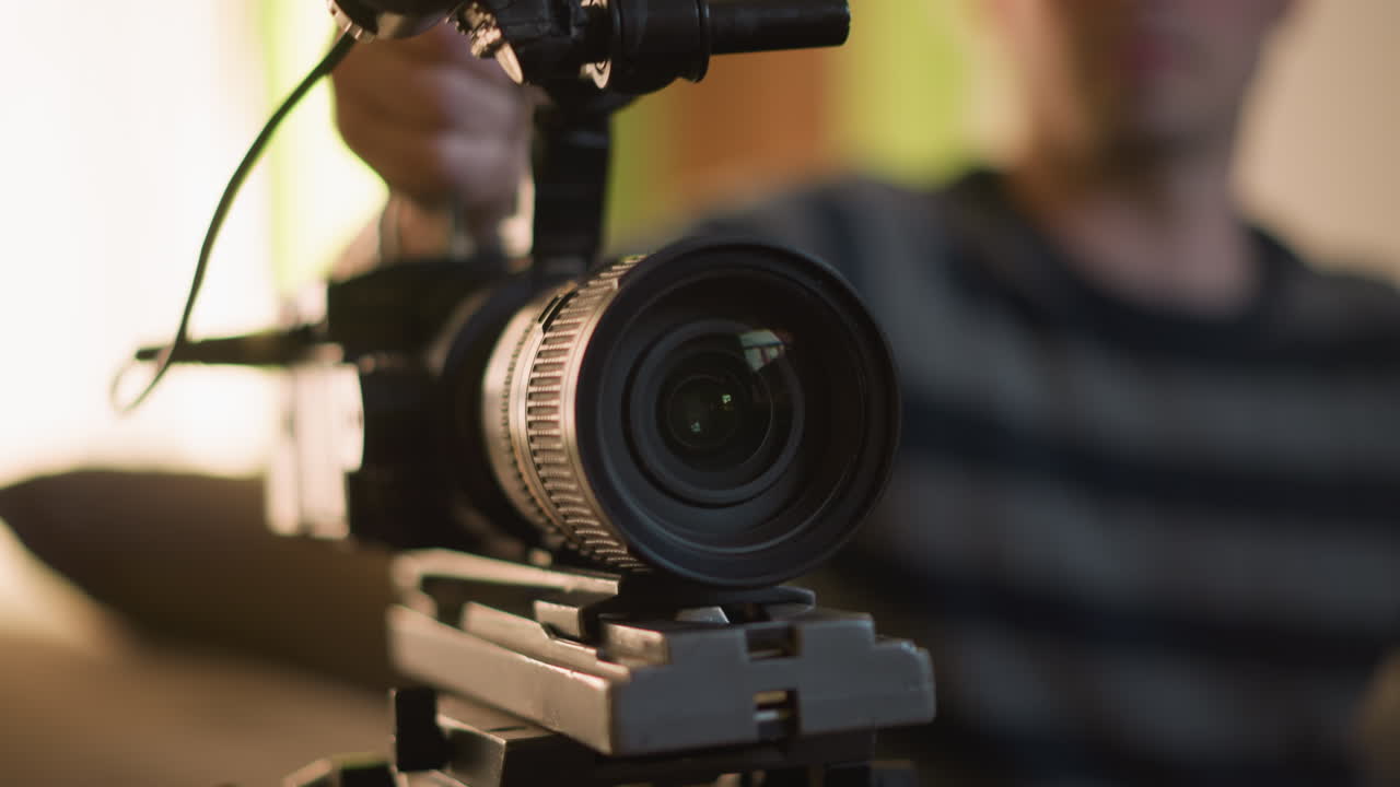 Close-up of camera tripod with focus on mounting plate, technician adjusting camera in background, green indoor environment with blurred details