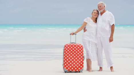 retired senior couple on beach with travel luggage