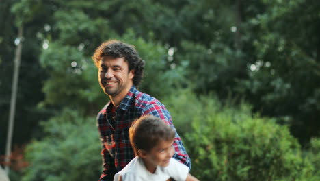 portrait of a young father and his little son playing on the backyard. dad is spinning the boy. blurred background