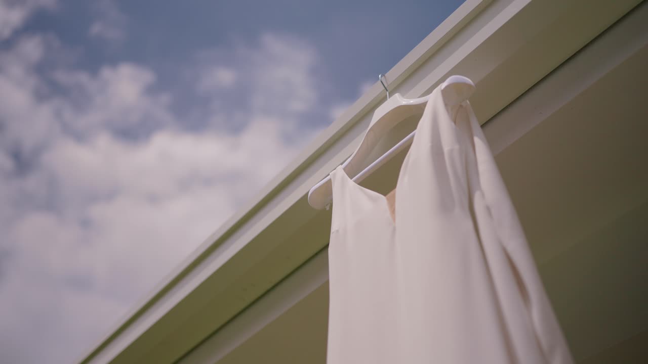 Elegant white wedding dress hanging on a hanger against a bright sky backdrop