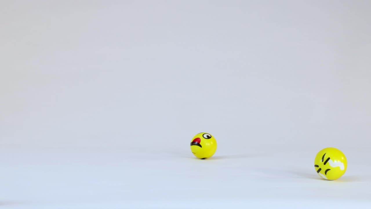 Diverse emoji gialle sferiche cadono, rimbalzano e rotolano sul pavimento pulito di uno studio bianco