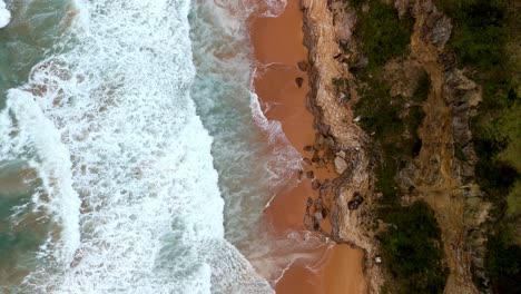 Vista-Aérea-De-Una-Ola-Rompiendo-En-Una-Playa-De-Arena-Dorada,-Los-Fascinantes-Patrones-De-Espuma-Y-Surf