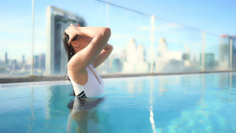 Después-De-Darse-Un-Chapuzón-En-La-Piscina-De-Un-Resort-En-La-Azotea,-Una-Mujer-Hermosa,-Saludable-Y-En-Forma-Se-Quita-El-Cabello-Mojado-De-La-Cara