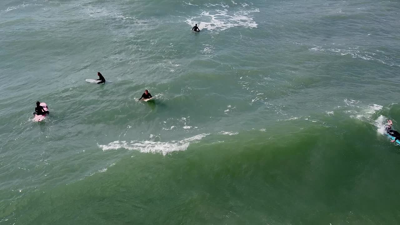 Group of surfers on boards waiting for waves near rocky shore, water activity, aerial view