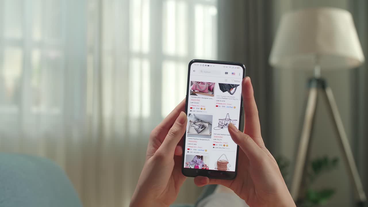 Close Up Of Hand Woman Lying On Couch In Living Room Using Smartphone Buys In Internet Shop. Female Looks At Goods In Online Store Bag. Buy Fashion Directly On Smartphone