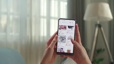 close up of hand woman lying on couch in living room using smartphone buys in internet shop. female looks at goods in online store bag. buy fashion directly on smartphone
