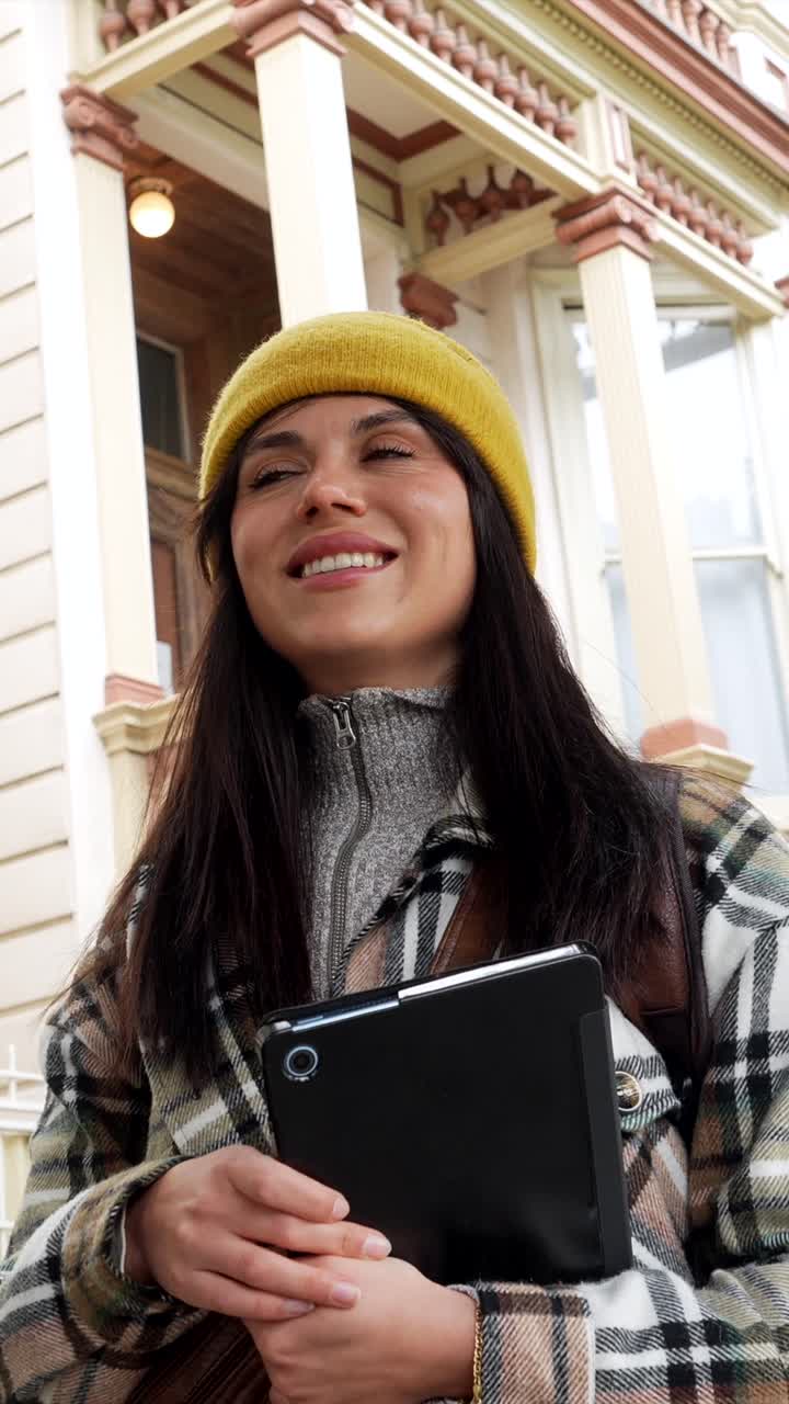 Donna sorridente con una giacca a quadri che tiene un tablet all'aperto.