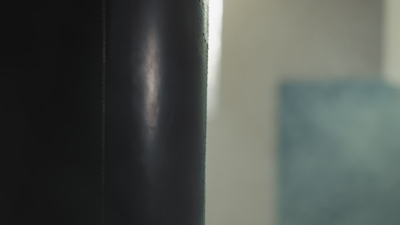 сильная рука мужчины в боевой перчатке делает удар по боевой сумке, демонстрируя силу. улучшение выносливости и физического здоровья в оборудованном помещении для спортсменов