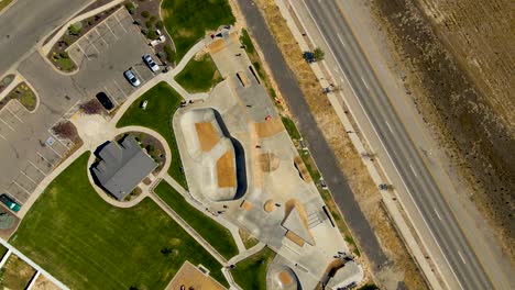 vertiginosa vista aérea giratoria de un parque de patinaje urbano lleno de niños divirtiéndose en verano