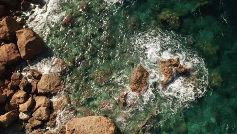 aerial tilt down reveal shot of a shore with beautiful red rocks and clear turquoise water and waves crushing on rocks on the beach near rampla beach on the island of gozo, malta