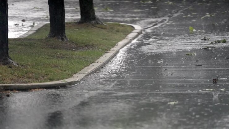Heavy rainfall splashing on asphalt road, adjacent to grassy curb